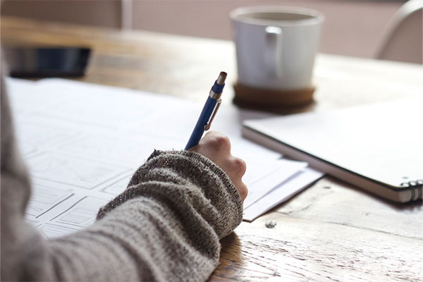 woman writing at a desk with pad and coffee mug