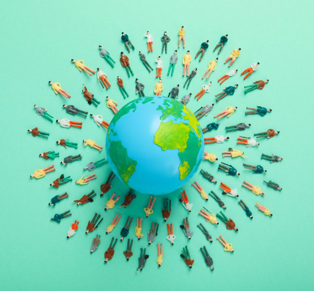 miniature people figures laying on a teal background surrounding a globe