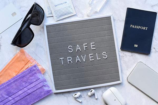 desk with travel items, masks, sunglasses, passport, air pods