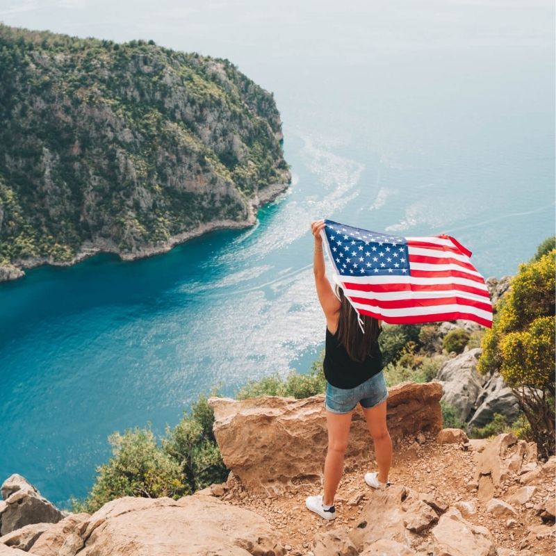 woman-celebrates-with-american-flag-on-scenic-coast